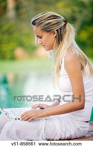 Young blonde woman sitting by the pool using laptop View Large Photo Image Stock Image - Young blonde woman sitting by the pool using laptop. Fotosearch
