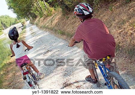Stock Image - Young boy and girl biking side by side, Carcassonne, Canal du Midi, France. Fotosearch