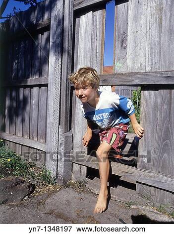 young boy climbing through a hole in the fence heading for adventure View Large Photo Image Stock Photo - young boy climbing through a hole in the fence heading for adventure. Fotosearch