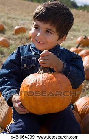 Stock Photo - Young boy holding pumpkin in pumpkin patch. Fotosearch