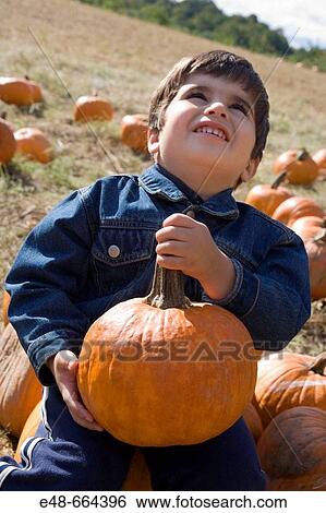 Stock Photograph - Young boy holding pumpkin in pumpkin patch. Fotosearch