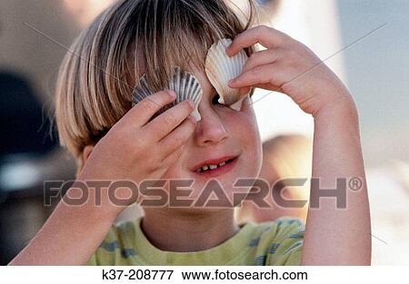 Young boy holding shells over his eyes View Large Photo Image Stock Photo - Young boy holding shells over his eyes. Fotosearch