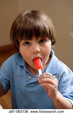Young boy in a blue shirt eating a red popsicle. View Large Photo Image Stock Photograph - Young boy in a blue shirt eating a red popsicle.. Fotosearch