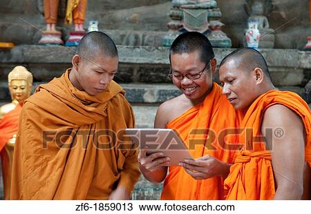 Stock Image - Young boy monks laughing and having fun at Apple Digital Tablet computer game in Siem Reap in Cambodia Asia relaxing and being boys. Fotosearch