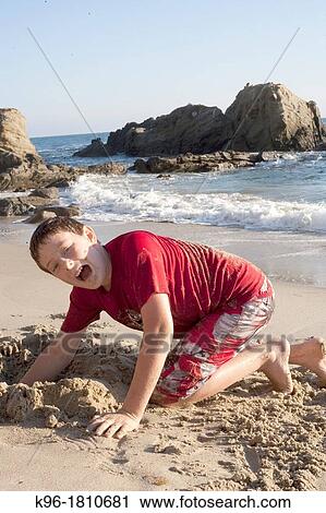 Stock Image - Young boy playing in the sand on a beach. Fotosearch