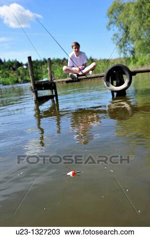 Stock Image - Young boy siting on a bridge fishing.. Fotosearch