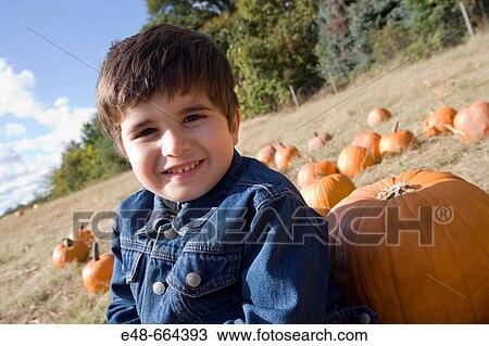 Young boy sitting by pumpkin in pumpkin patch View Large Photo Image Stock Image - Young boy sitting by pumpkin in pumpkin patch. Fotosearch