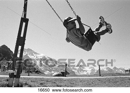 Young boy swings a high arc on chain link swing in the Swiss Alps with mountain peaks behind and cows sitting patiently below View Large Photo Image Stock Image - Young boy swings a high arc on chain link swing in the Swiss Alps with mountain peaks behind and cows sitting patiently below. Fotosearch