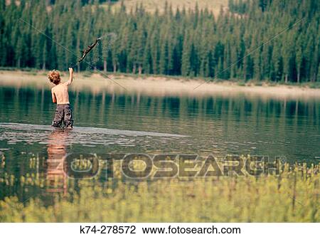 Stock Image - Young Boy Throwing Stick In Lake. Kananaskis, Canada. Fotosearch