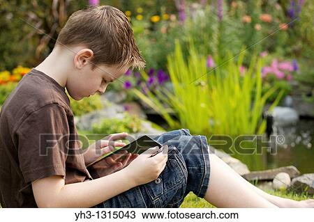 Young boy using an iPad in the garden View Large Photo Image Stock Image - Young boy using an iPad in the garden. Fotosearch