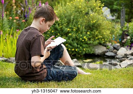 Young boy using an iPad in the garden View Large Photo Image Stock Photo - Young boy using an iPad in the garden. Fotosearch