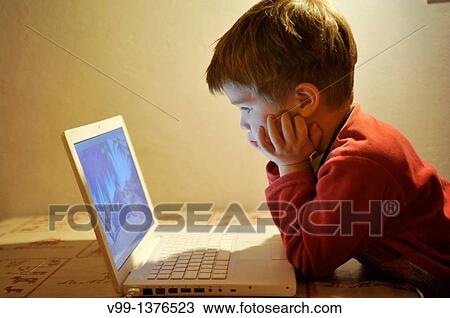 Stock Image - young boy who watches a movie on the computer. Fotosearch