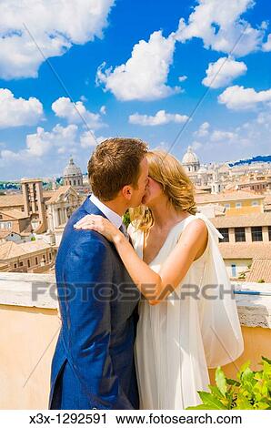 Stock Image - Young bride and groom kissing on rooftop in Rome, Italy. Fotosearch