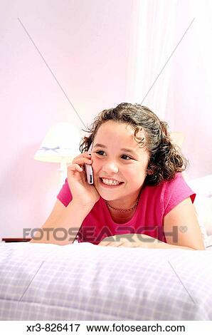 Young brunette child laying on bed while talking on a pink cell phone View Large Photo Image Stock Photo - Young brunette child laying on bed while talking on a pink cell phone. Fotosearch