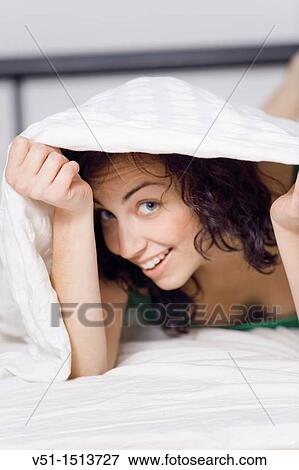 Stock Photo - Young brunette woman hiding under the sheets. Fotosearch