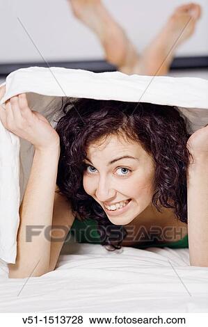 Stock Photo - Young brunette woman hiding under the sheets. Fotosearch