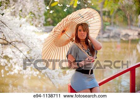 Young brunette woman in a mini-skirt in a garden setting holding a parasol looking at the camera. View Large Photo Image Stock Image - Young brunette woman in a mini-skirt in a garden setting holding a parasol looking at the camera.. Fotosearch