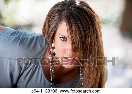 Stock Photograph - Young brunette woman in a mini-skirt in a garden setting looking directly at the camera.. Fotosearch