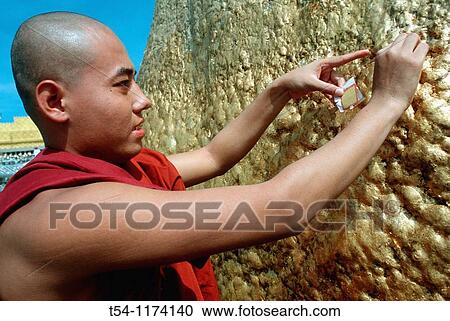 Stock Image - young Buddhist monk responsible gold leaf on the golden rock. Fotosearch