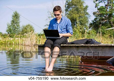 Young business man sitting at a pond with his laptop computer View Large Photo Image Stock Image - Young business man sitting at a pond with his laptop computer. Fotosearch