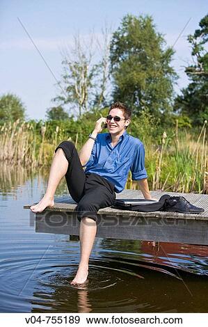 Young business man using his cell phone at a pond View Large Photo Image Stock Photo - Young business man using his cell phone at a pond. Fotosearch