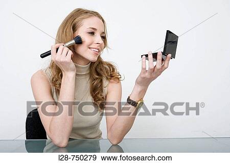 Stock Photo - Young business woman applying make-up to face, portrait, close-up. Fotosearch
