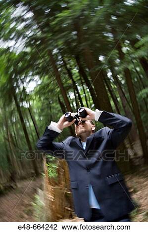 Stock Image - Young businessman in forest looking through binoculars. Fotosearch