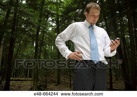 Picture - Young businessman in forest with cellular phone. Fotosearch