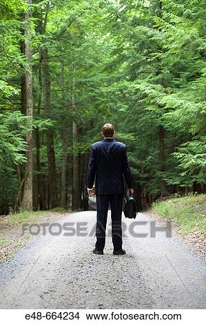 Picture - Young businessman standing in forest on dirt road with briefcase. Fotosearch