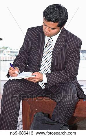 Young businessman writing on papers while working outside of the office View Large Photo Image Stock Image - Young businessman writing on papers while working outside of the office. Fotosearch