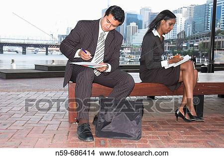 Young businesspeople filling in paperwork while working out of the office View Large Photo Image Picture - Young businesspeople filling in paperwork while working out of the office. Fotosearch