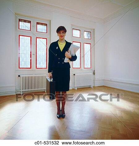Stock Image - Young businesswoman with black dress standing in empty room. Fotosearch