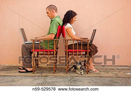 Young casual couple using laptop computers. Sitting outside back to back with small dog. View Large Photo Image Stock Photo - Young casual couple using laptop computers. Sitting outside back to back with small dog.. Fotosearch