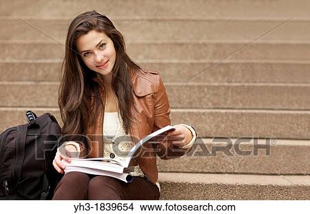 Picture - Young caucasian girl reading textbook at a university library. Fotosearch
