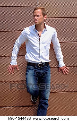 Young caucasian man, full body, with white shirt and jeans, looking friendly into the far distance while leaning at a metal wall, Hamburg, Germany, Europe View Large Photo Image Stock Image - Young caucasian man, full body, with white shirt and jeans, looking friendly into the far distance while leaning at a metal wall, Hamburg, Germany, Europe. Fotosearch