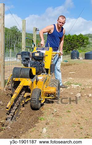 Young Caucasian man of 24 years is operating a walk-behind trencher to make a ditch for pipes and cable View Large Photo Image Stock Photo - Young Caucasian man of 24 years is operating a walk-behind trencher to make a ditch for pipes and cable. Fotosearch