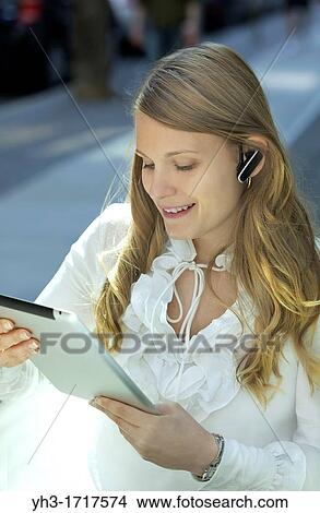 Young Caucasian woman wearing a Blutooth headset while using digital tablet View Large Photo Image Picture - Young Caucasian woman wearing a Blutooth headset while using digital tablet. Fotosearch