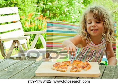 Stock Image - Young child, four year old girl, eating pizza outside in the garden. Fotosearch