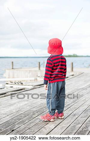 Young child wearing casual clothes and a red hat watching the sea from a wooden jetty View Large Photo Image Stock Image - Young child wearing casual clothes and a red hat watching the sea from a wooden jetty. Fotosearch