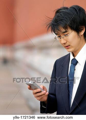 Stock Photograph - young Chinese man using his mobile phone to communicate and perform business transactions. Fotosearch