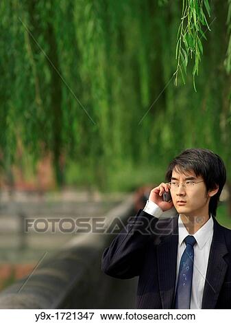 Stock Photo - young Chinese man using his portable phone to communicate and perform business transactions. Fotosearch
