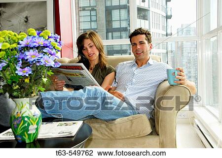 young couple at home on sofa reading newspaper View Large Photo Image Stock Image - young couple at home on sofa reading newspaper. Fotosearch