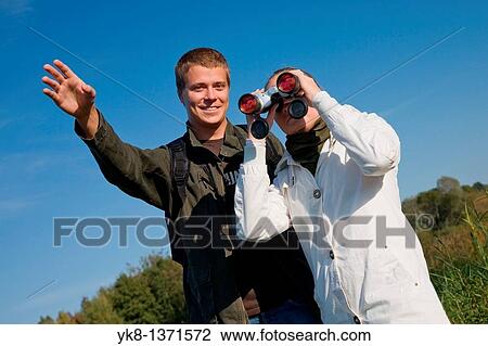 Stock Image - Young couple birdwatching with binoculars pointing away. Fotosearch