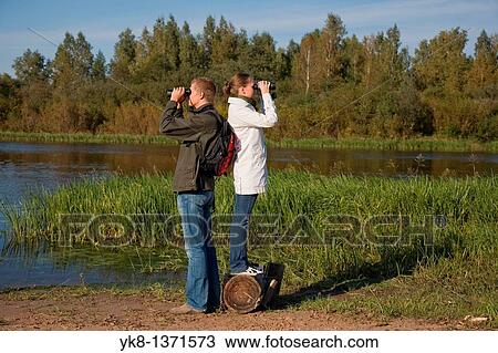 Young couple birdwatching with binoculars by river water View Large Photo Image Stock Image - Young couple birdwatching with binoculars by river water. Fotosearch