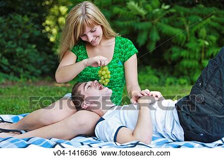 Stock Photograph - Young couple eating grapes in the garden, smiling, Germany, Europe. Fotosearch