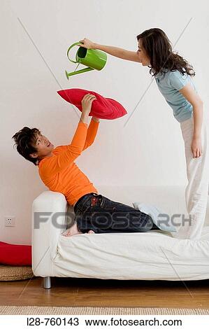 Stock Image - Young couple having pillow fight in sofa. Fotosearch