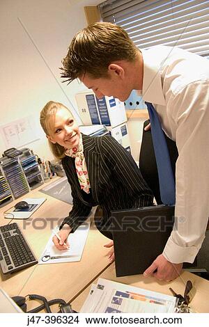 Young couple, in an office, working at a desk smiling at each other View Large Photo Image Picture - Young couple, in an office, working at a desk smiling at each other. Fotosearch