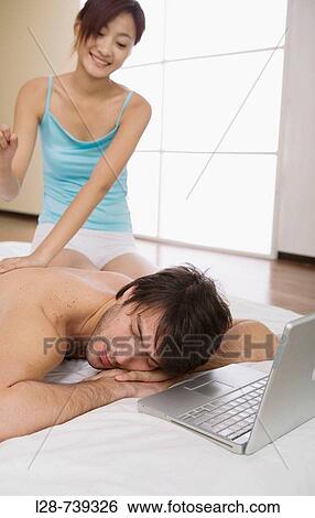 Stock Photograph - Young couple in bedroom, woman massaging man,. Fotosearch
