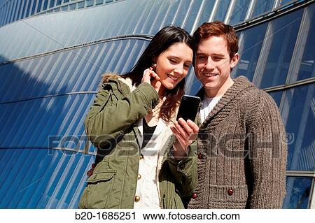Young couple looking at mobile phone in the city, smartphone, Iberdrola Tower, Abandoibarra, Bilbao, Bizkaia, Basque Country, Spain View Large Photo Image Stock Image - Young couple looking at mobile phone in the city, smartphone, Iberdrola Tower, Abandoibarra, Bilbao, Bizkaia, Basque Country, Spain. Fotosearch