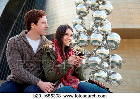 Young couple looking at mobile phone in the city, smartphone, Guggenheim Museum, Abandoibarra, Bilbao, Bizkaia, Basque Country, Spain View Large Photo Image Stock Photo - Young couple looking at mobile phone in the city, smartphone, Guggenheim Museum, Abandoibarra, Bilbao, Bizkaia, Basque Country, Spain. Fotosearch